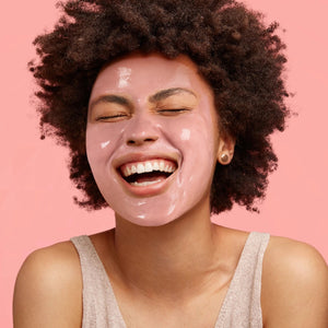 Woman with a white facial mask applied, smiling with eyes closed
