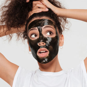 Woman applying a black facial mask across forehead and cheeks