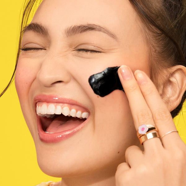 Facial mask application: person smooths black peel-off mask on face near cheek.