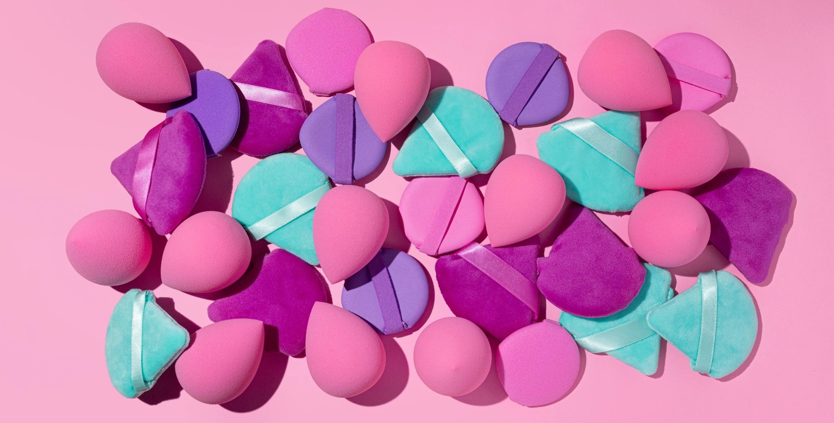 Assorted plush heart shapes with satin ribbons in pink, purple, and teal on a light pink background