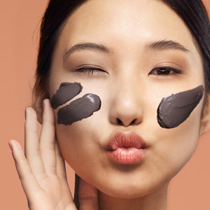 Face with dark brown cacao cream mask smeared on cheeks and forehead, eyes closed