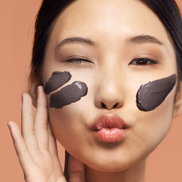 Face with dark brown cacao cream mask smeared on cheeks and forehead, eyes closed