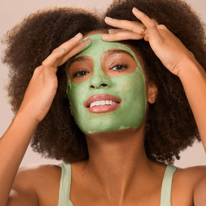Person wearing green matcha cream mask on face, smoothing with hands