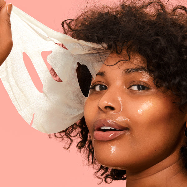 Sheet face mask and black under-eye patches on a woman's face, skincare set.