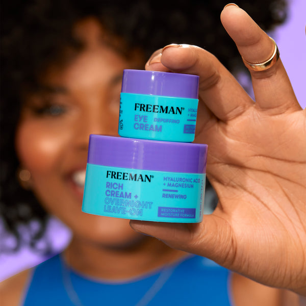 Hands holding two Freeman rich overnight leave-on cream jars, blue and purple