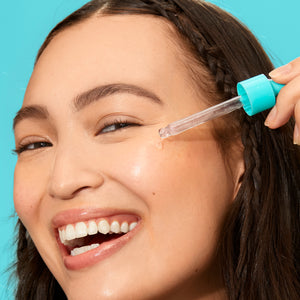 Glow serum dropper applying clear gel onto a cheek