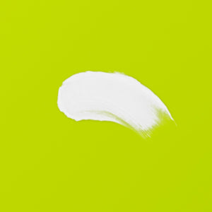 White cleansing balm smear on green surface, product texture detail.